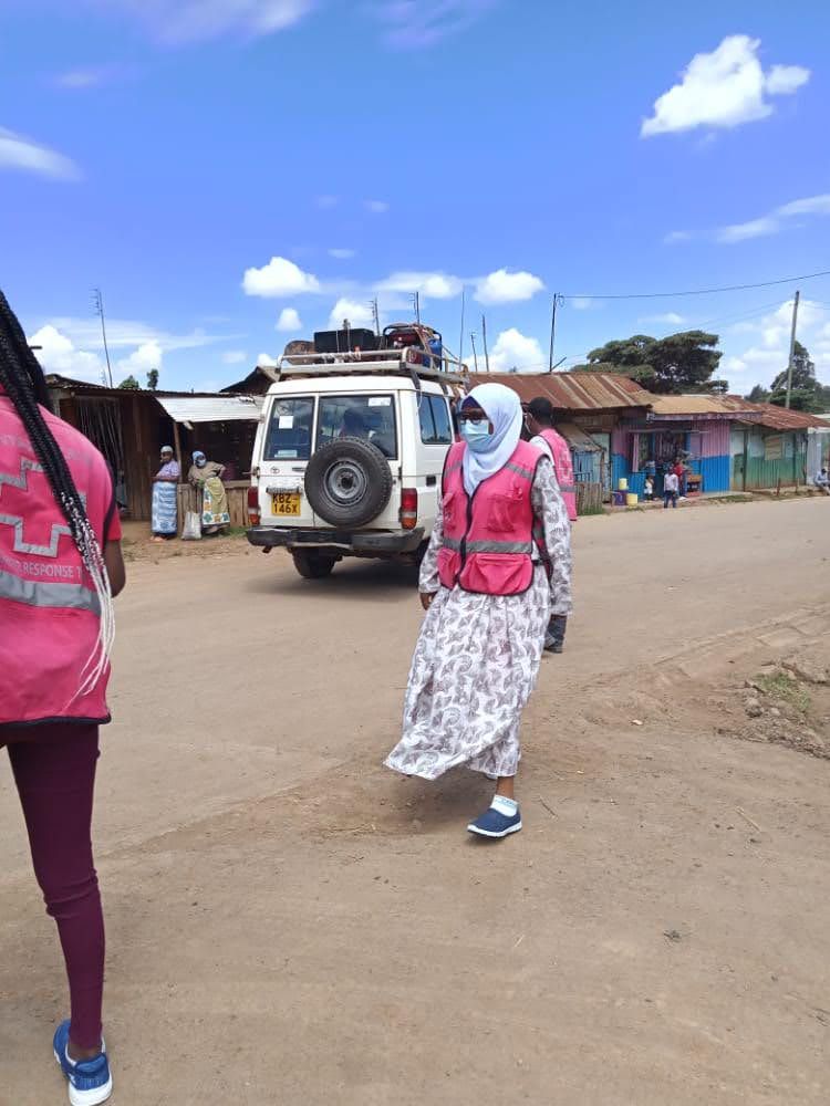 A Beautiful Minds Network team member in a Red Cross-branded vest walking through a community during a psychosocial support outreach